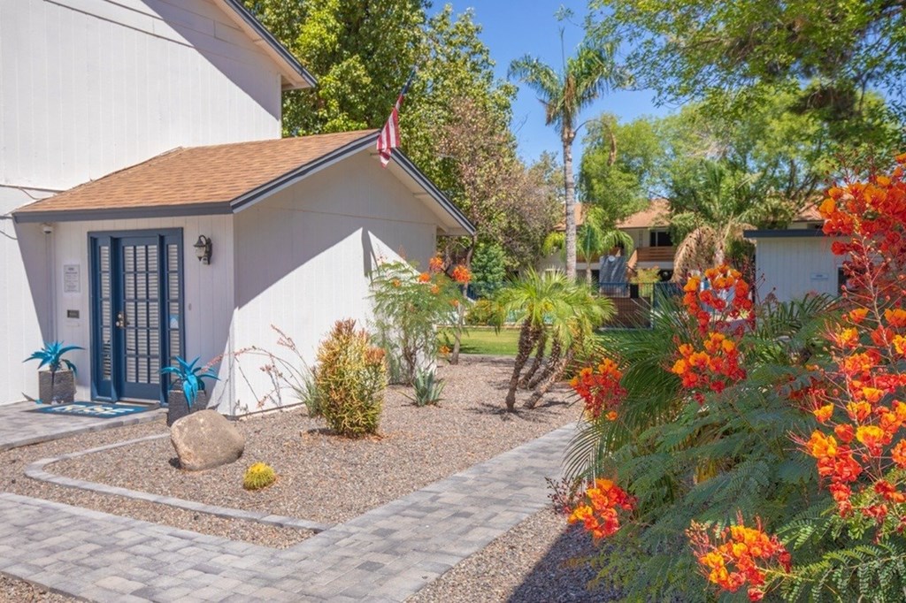 A white house with a flag on the front and a garden with red flowers.