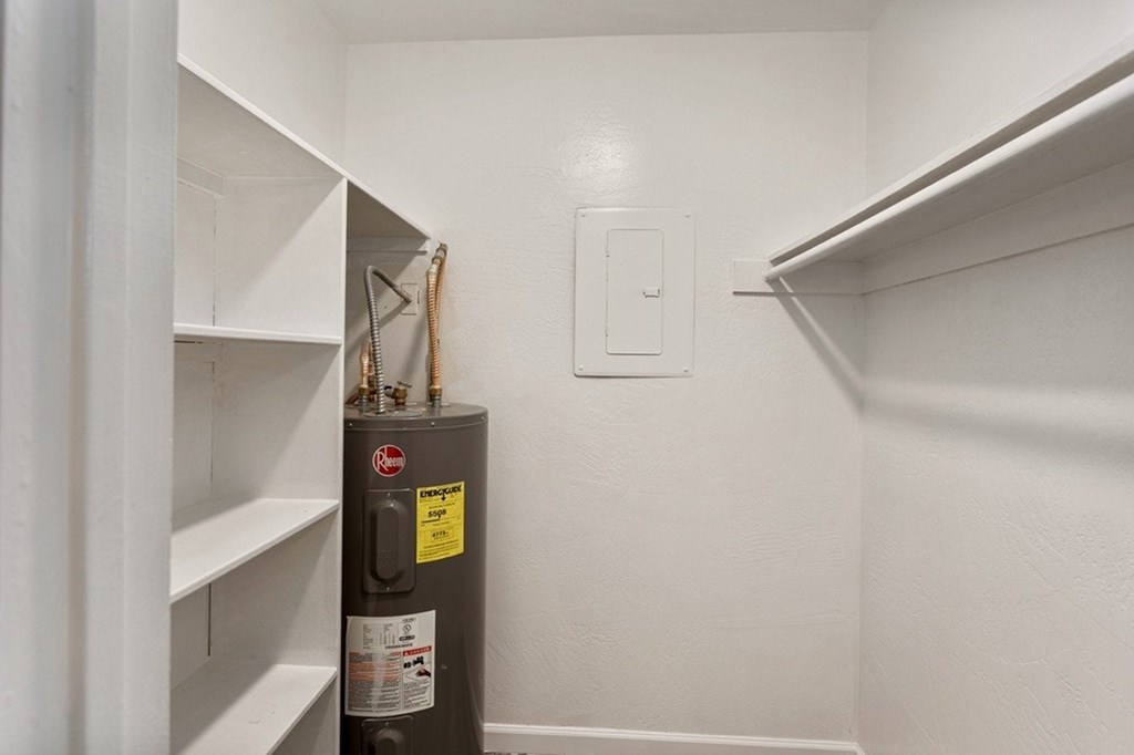 A small, white closet with a metal storage unit and a light switch.