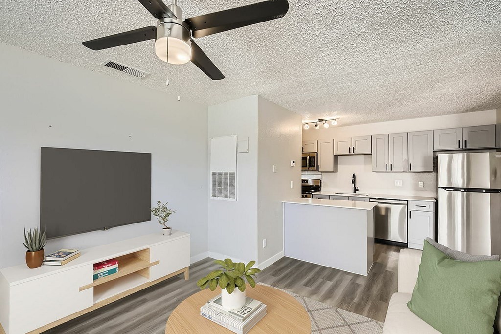 A modern living room with a flat screen TV, a coffee table, and a kitchen in the background.