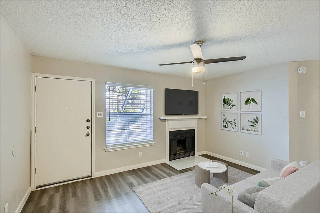 A living room with a fireplace, a television, and a ceiling fan.