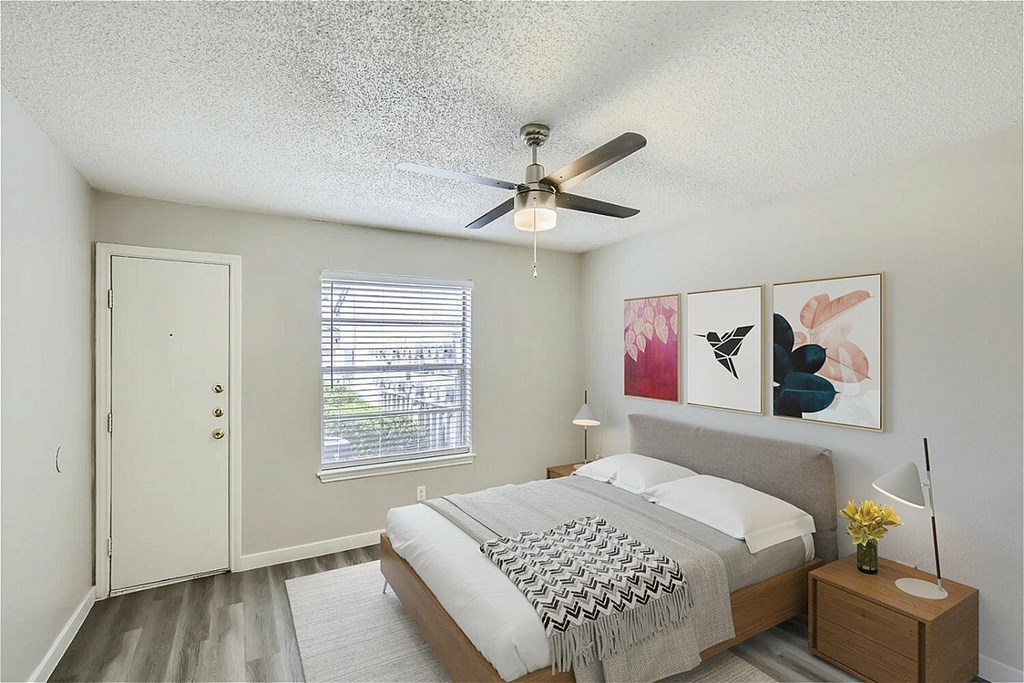 A bedroom with a bed, a ceiling fan, and a painting on the wall.
