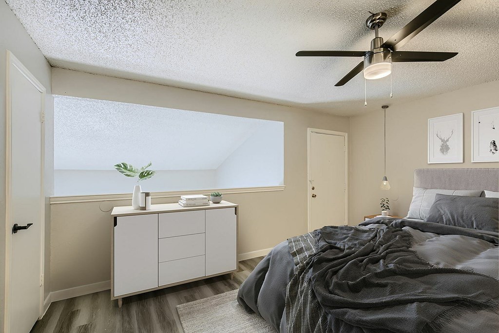 A bedroom with a bed, a ceiling fan, and a cabinet with a plant on top.