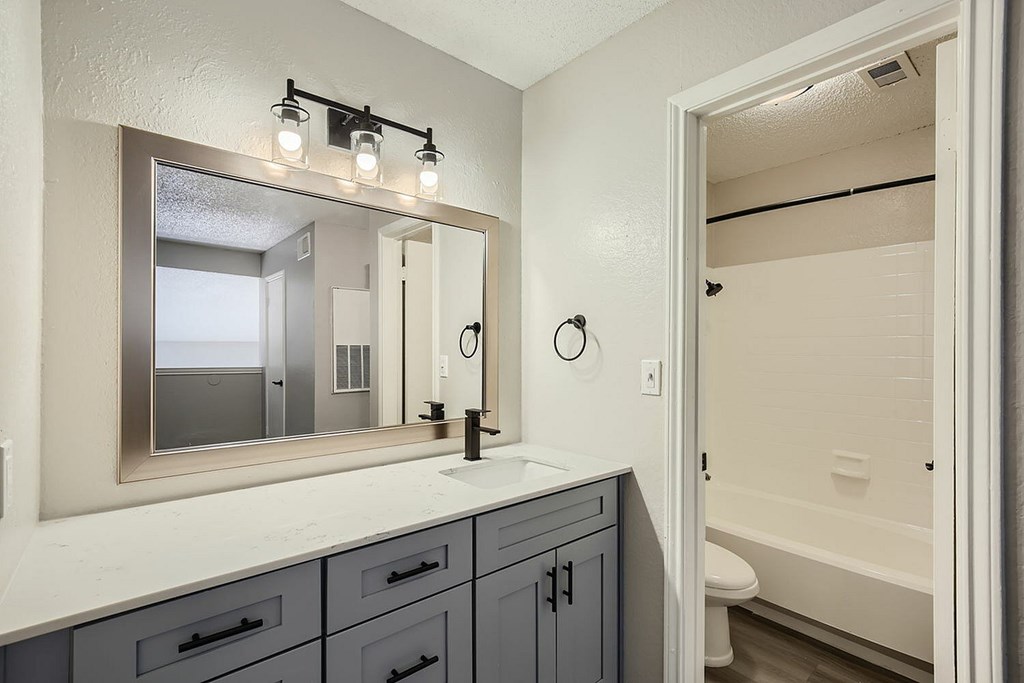 A bathroom with a mirror, lights, and a toilet.