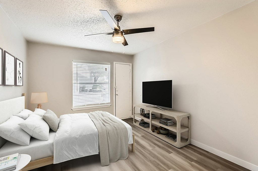 A bedroom with a bed, a television, and a ceiling fan.