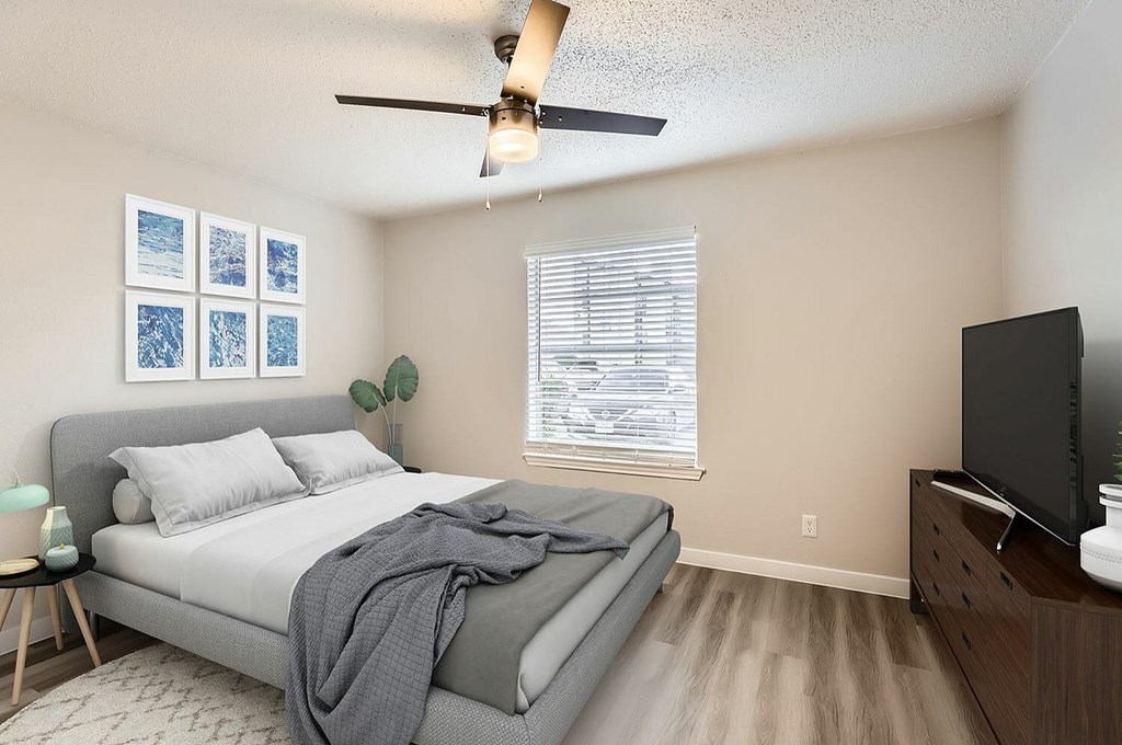 A bedroom with a bed, a ceiling fan, a television, and a window with blinds.