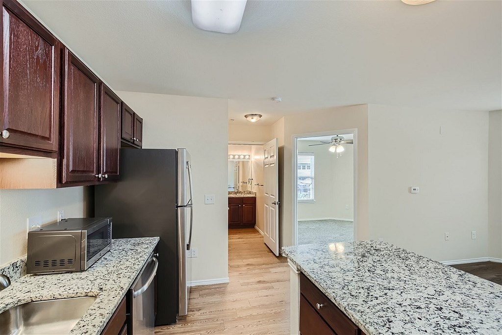 A kitchen with a black refrigerator and a microwave on a granite countertop.