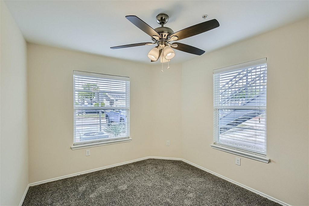 A room with a ceiling fan and two windows.