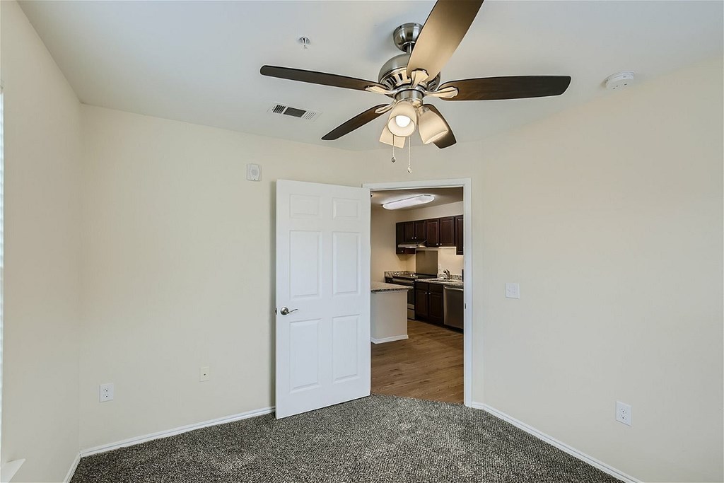 A room with a ceiling fan and a door leading to a kitchen.