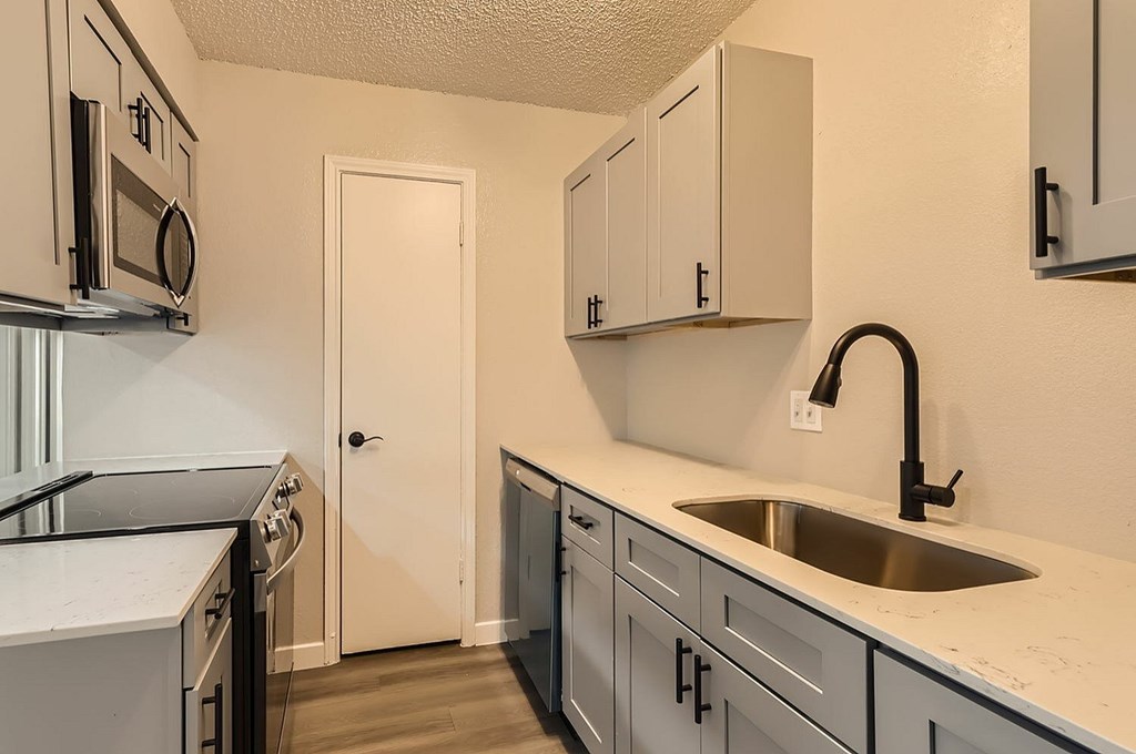 A kitchen with a sink, stove, and cabinets.