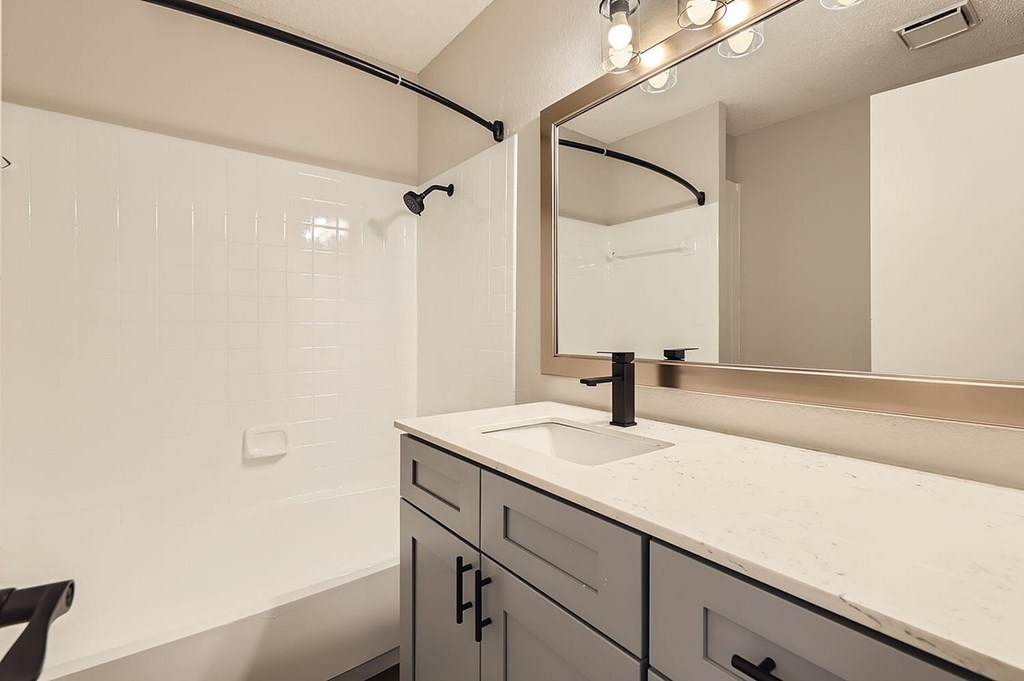 A bathroom with a sink, mirror, and lighting fixtures.