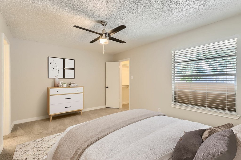 A bedroom with a bed, dresser, and window with blinds.
