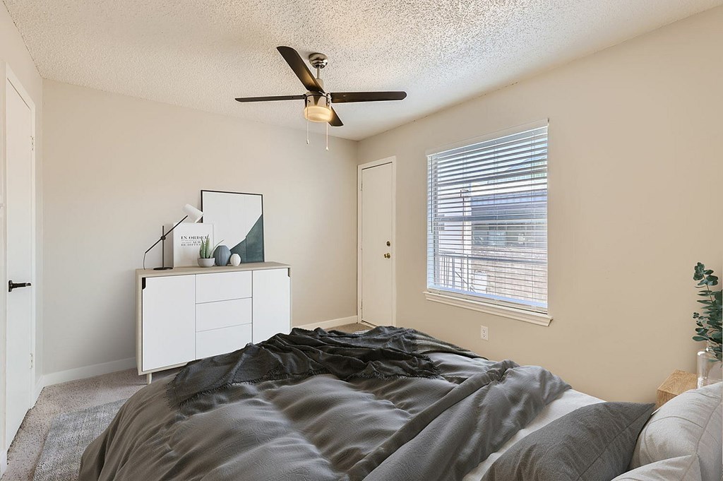 A bedroom with a bed, a ceiling fan, and a window with blinds.