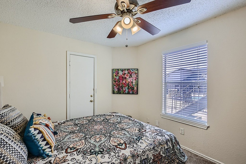 A bedroom with a bed, pillows, a ceiling fan, and a window with blinds.
