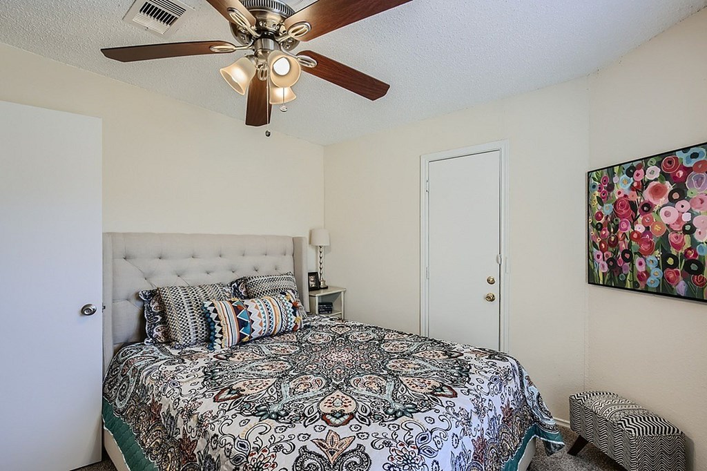 A bedroom with a bed, a ceiling fan, and a painting on the wall.