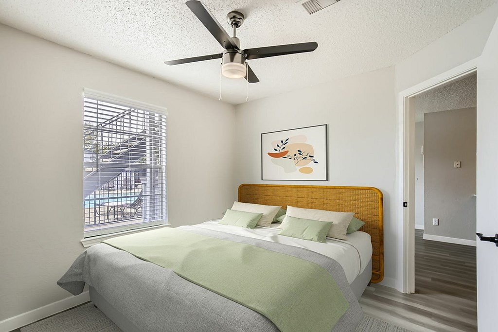 A bedroom with a bed, a ceiling fan, and a window with blinds.