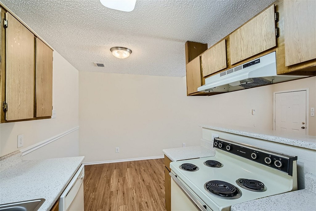 A kitchen with a white stove top oven and wooden cabinets.