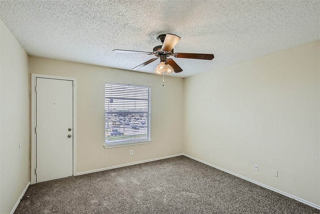 A room with a ceiling fan and a window overlooking a parking lot.