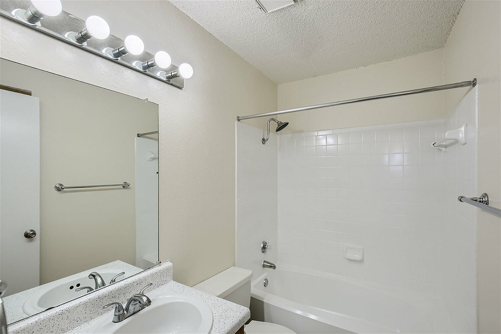 A white bathroom with a sink, mirror, and bathtub.