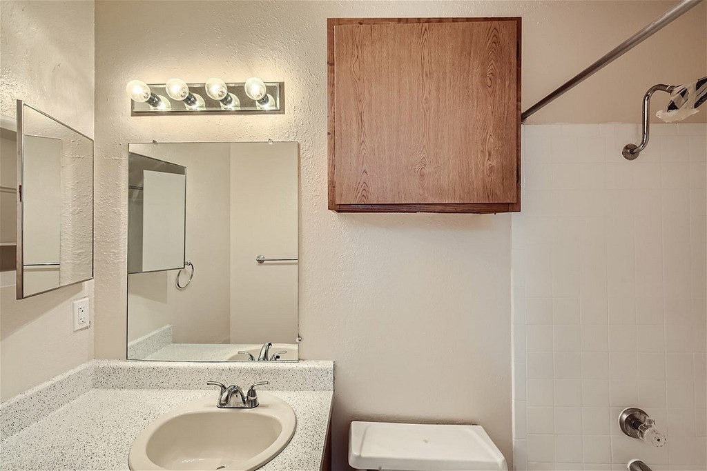 A bathroom with a sink, mirror, toilet and shower.