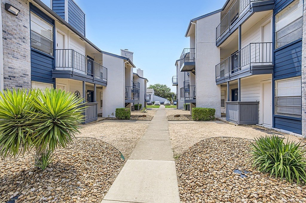 A sunny day at a residential area with apartment buildings and a gravel path.
