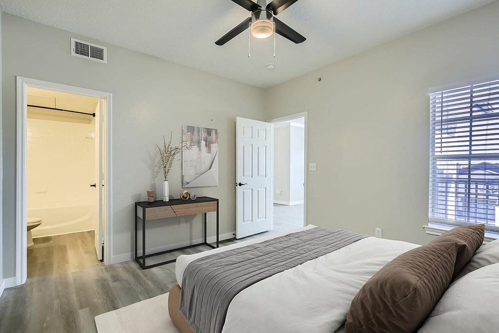 A bedroom with a bed, a table with a vase and candles, and a ceiling fan.