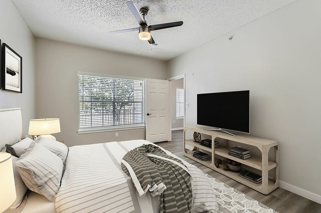 A bedroom with a bed, a television, and a ceiling fan.