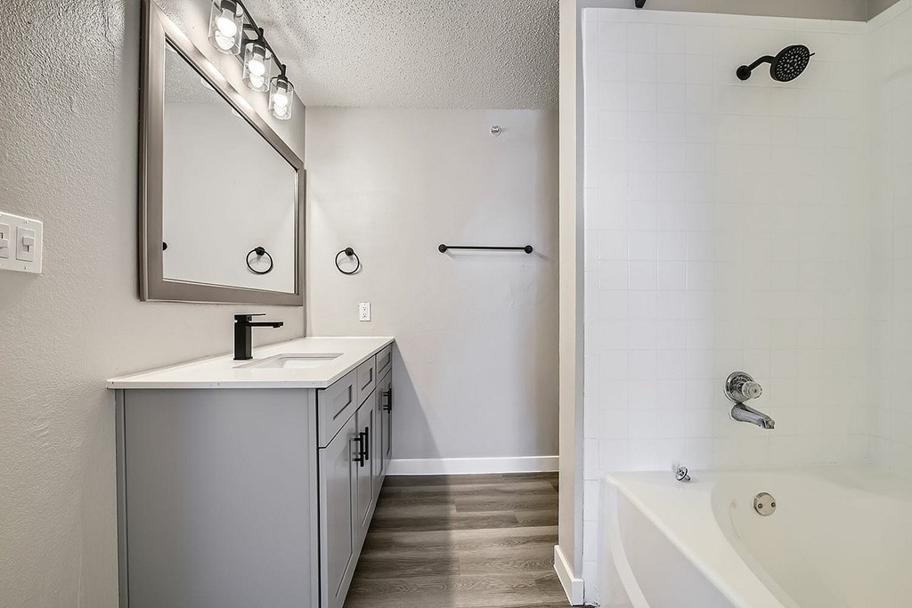 A white bathroom with a sink, mirror, and bathtub.