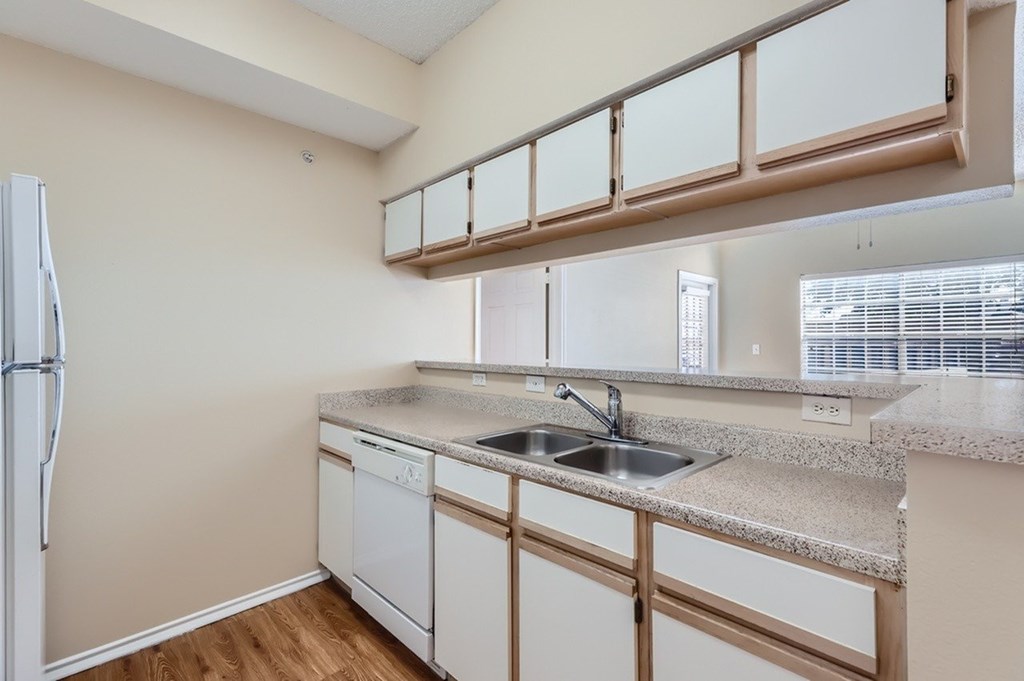 A kitchen with a white fridge, white dishwasher, and a granite countertop.