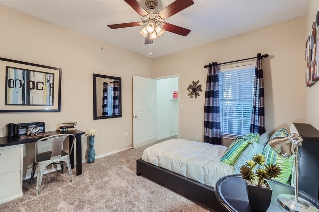 A bedroom with a bed, desk, chair, and a ceiling fan.