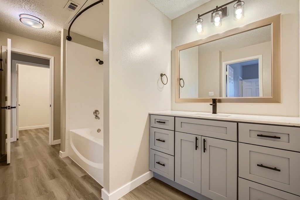 A bathroom with a white tub and grey cabinets.
