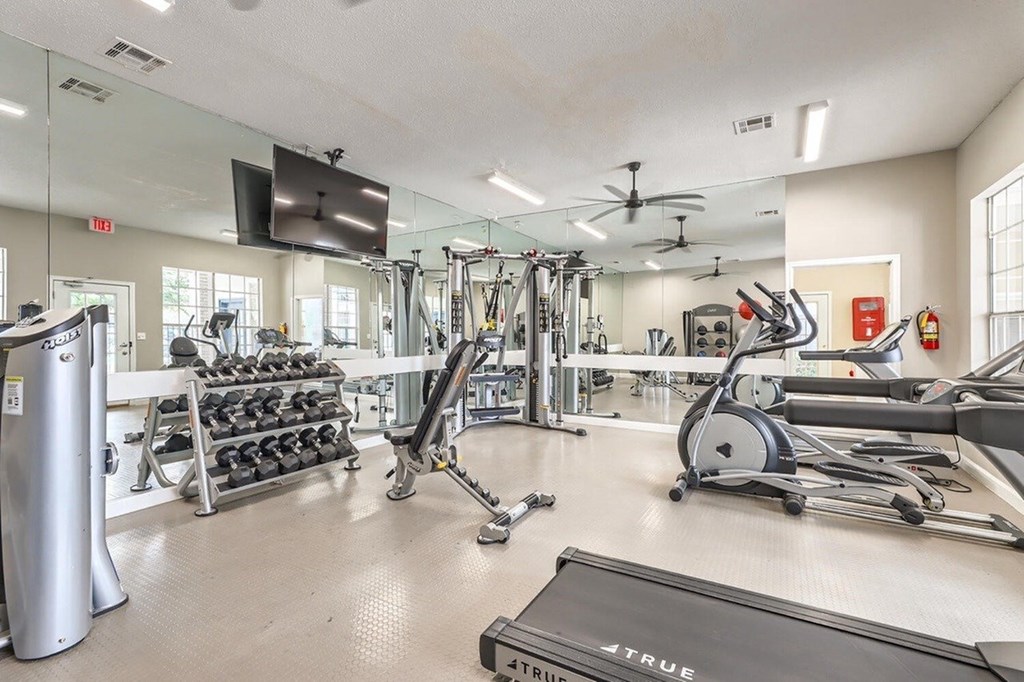 A gym with a variety of equipment including treadmills, weights, and exercise machines.