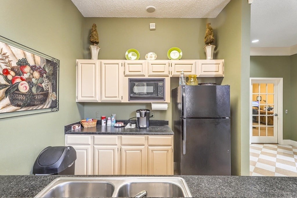 A kitchen with a black refrigerator and a black trash can.