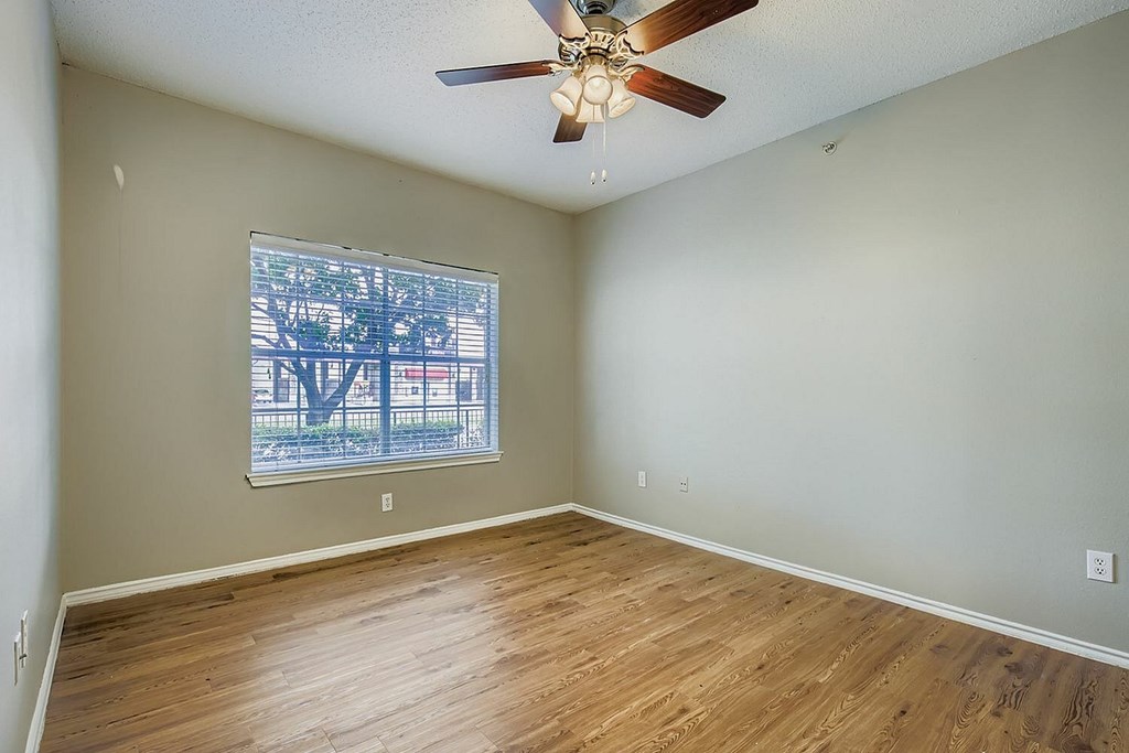A room with a ceiling fan and a window showing a view of a city.