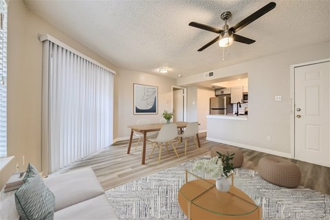 A living room with a ceiling fan and a dining table with chairs.