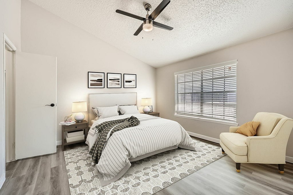 A bedroom with a bed, chair, and ceiling fan.