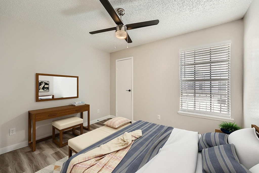 A bedroom with a bed, desk, and window with blinds.