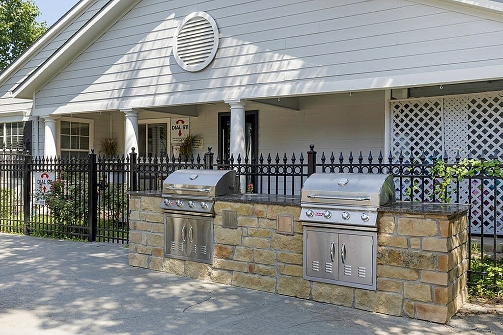 A white house with a stone wall and a grill on it.