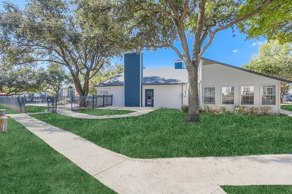 A white building with a blue door is surrounded by a white fence and green grass.