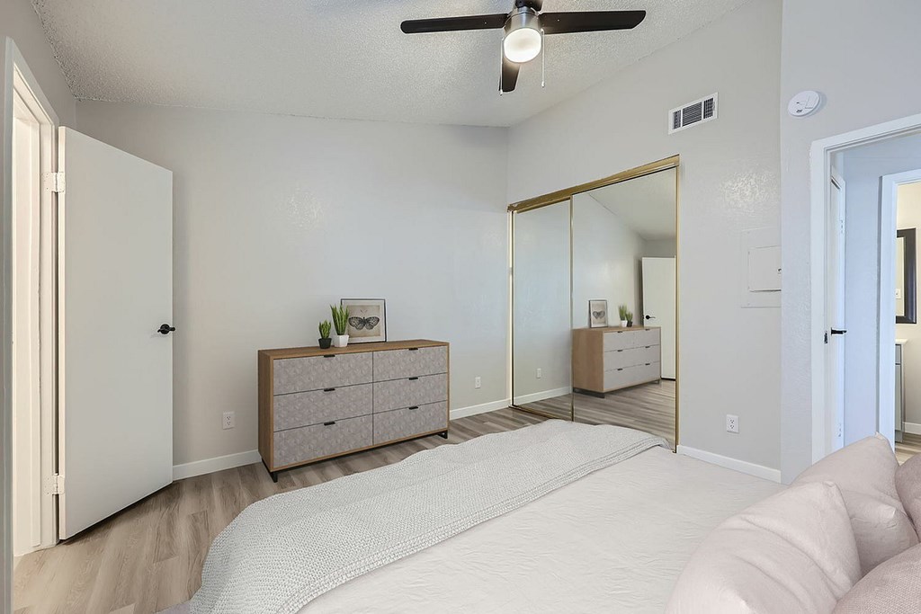A bedroom with a bed, dresser, mirror, and ceiling fan.