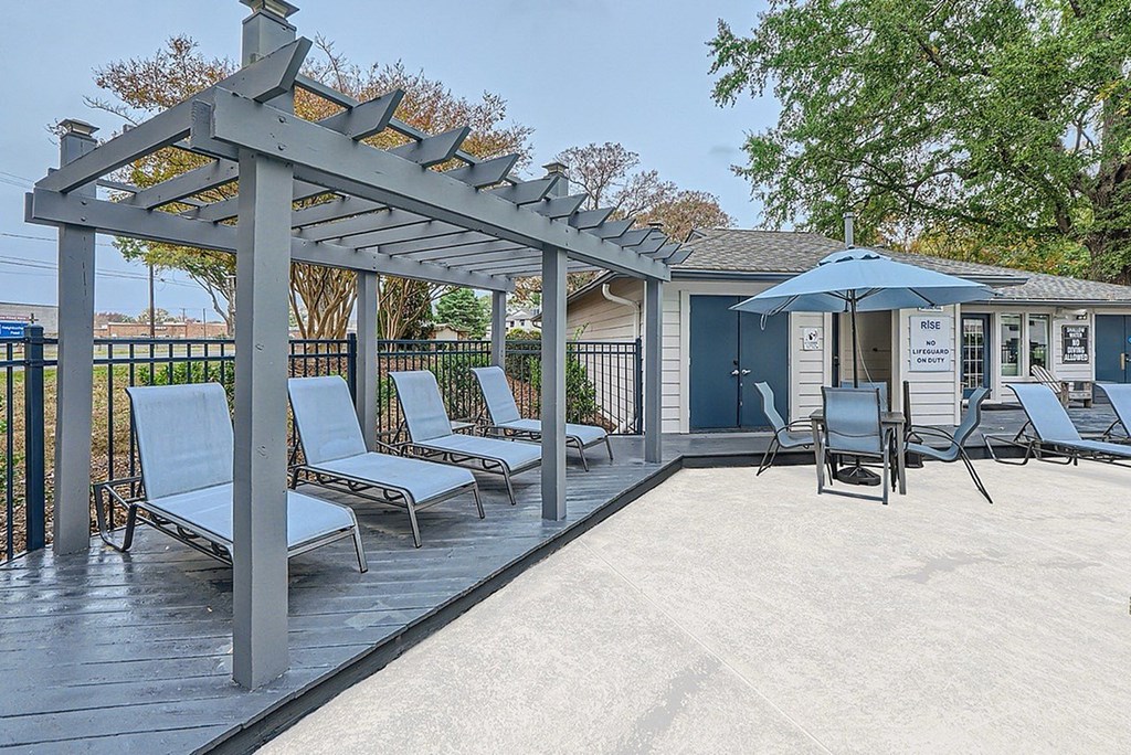 A patio with a pergola and chairs.