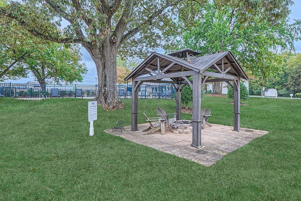A wooden pavilion with a sign in front of a tree.