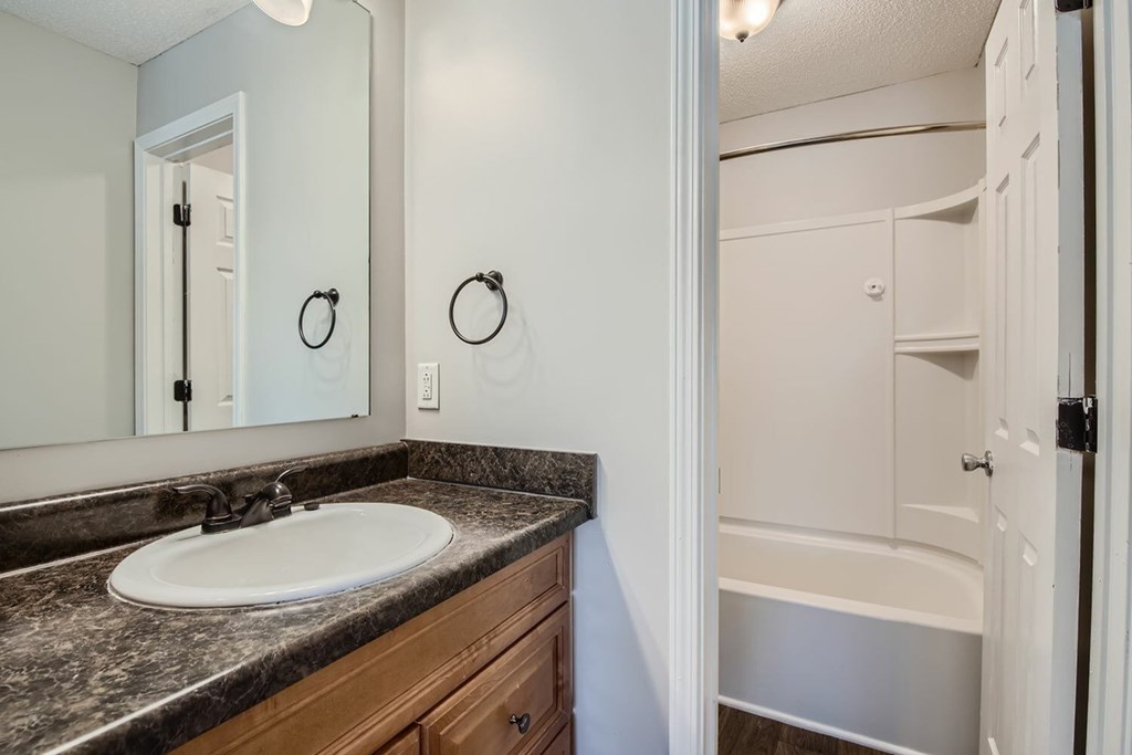 A bathroom with a sink, mirror, and bathtub.