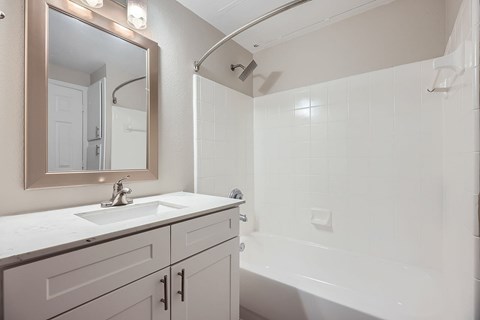 A white bathroom with a sink, mirror, and shower.