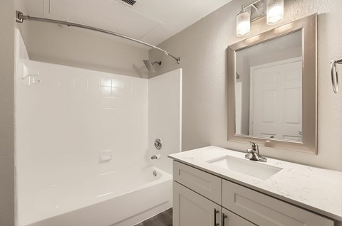 A white bathroom with a white tub, sink, and mirror.