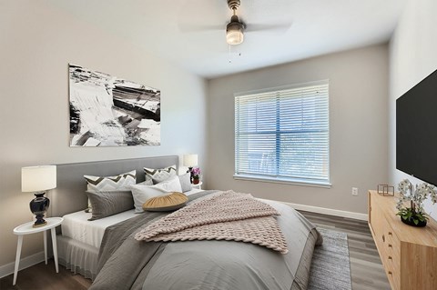 A bedroom with a large bed, a ceiling fan, and a painting on the wall.