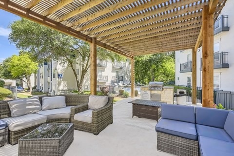 A patio with a wooden pergola and wicker furniture.