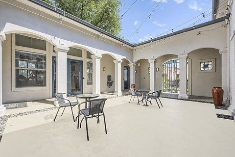 A patio with a table and chairs is surrounded by a white building with arches.