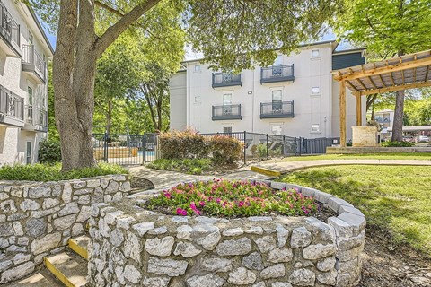 A stone wall with flowers in front of apartment buildings.