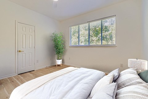 A bedroom with a large bed and a potted plant by the window.
