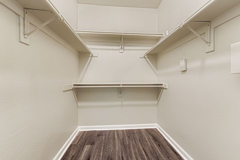 A walk-in closet with white walls and wood flooring.